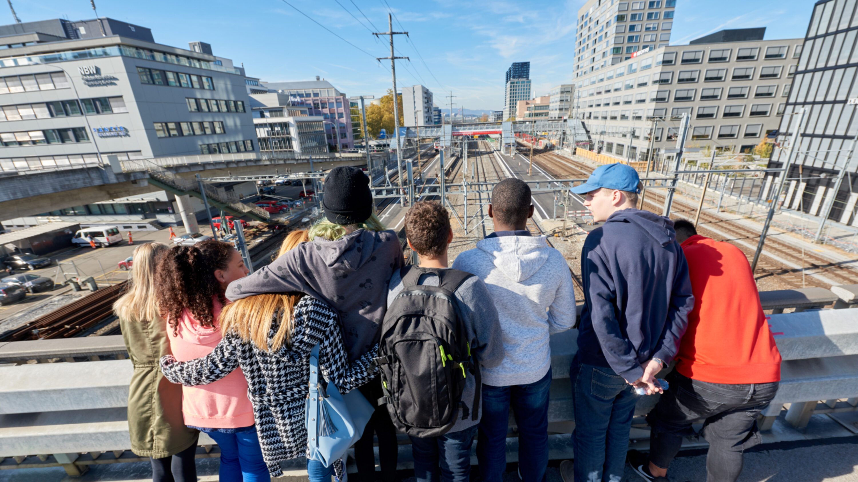 Jugendgruppe blickt auf Bahngleise in städtischer Umgebung.