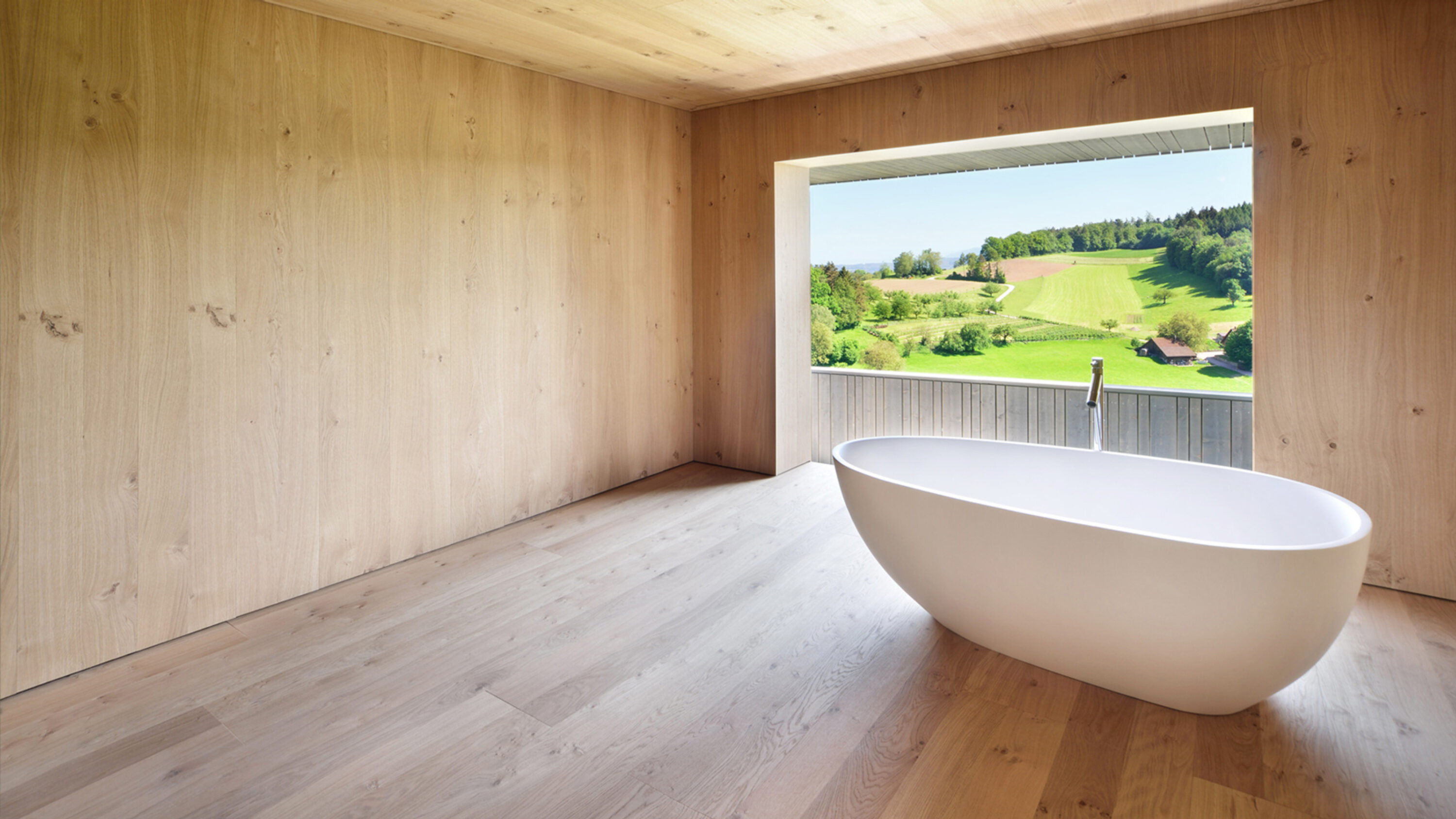 Minimalistischer Raum mit freistehender Badewanne und Blick auf grüne Landschaft