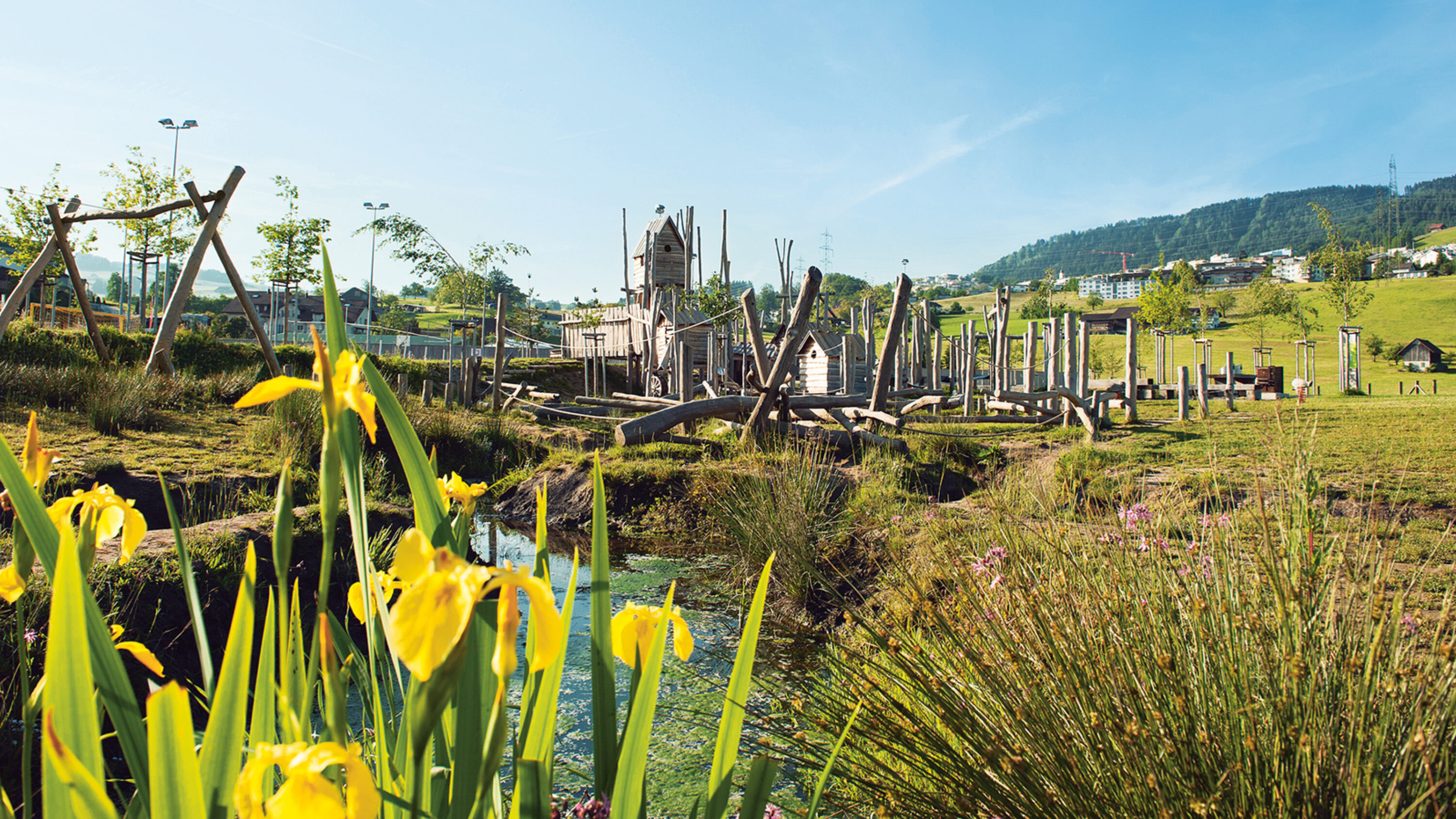 Naturspielplatz mit Holzgeräten und blühender Landschaft.