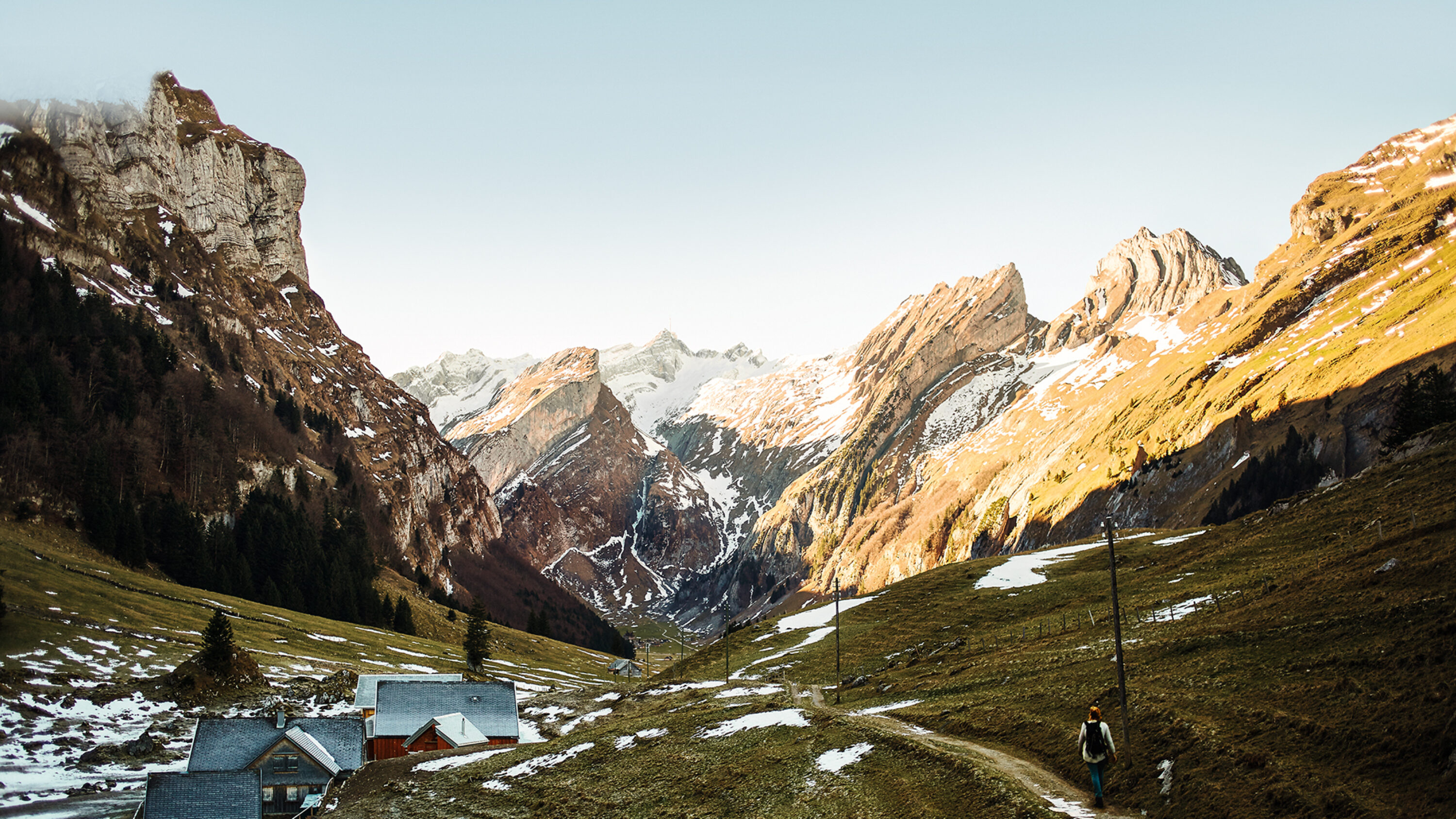 Alpenlandschaft mit Berghütten und Wanderin auf einem Pfad